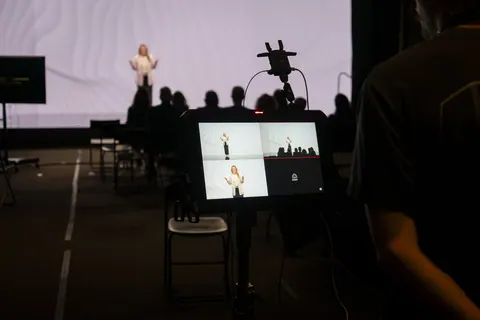 A camera filming a speaker onstage in a live room.